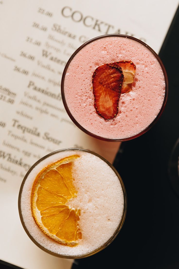 two drinks sitting on top of a table next to an open book and orange slice