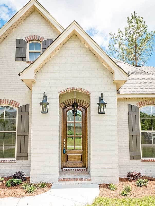 a white brick house with brown shutters and two large windows on the front door