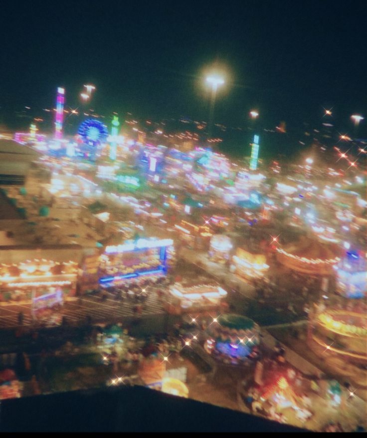 an aerial view of a carnival at night with lights and rides in the foreground