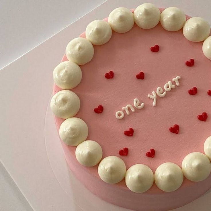 a pink cake with white frosting and red hearts on it that says one year