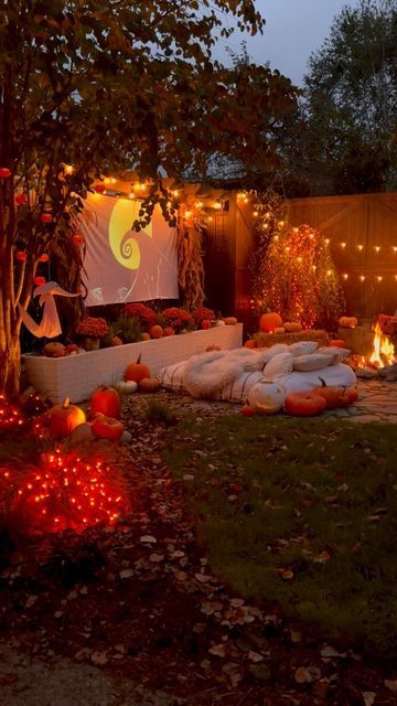 a backyard with pumpkins and lights on the ground in front of a movie screen