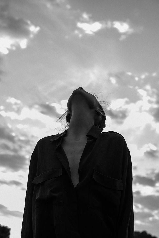 black and white photograph of woman in front of cloudy sky with sun peeking through clouds