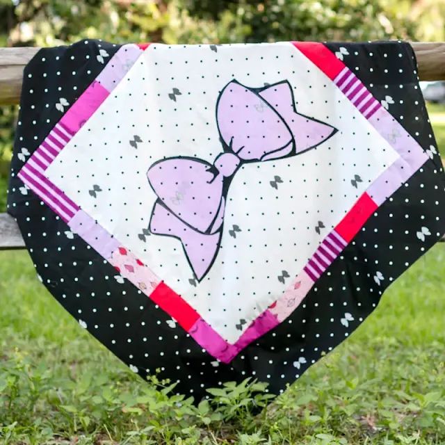 a black and white quilt with a pink bow on it sitting on top of a wooden bench