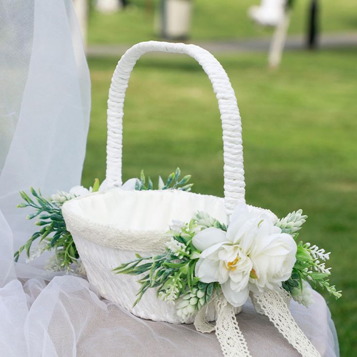 a white basket with flowers and greenery on the back is sitting on a pillow