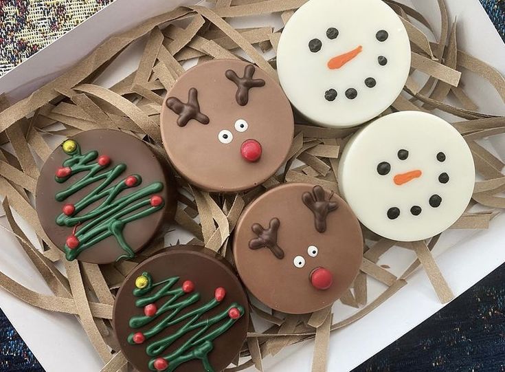 four decorated cookies in a box on top of some brown and white paper with snowmen