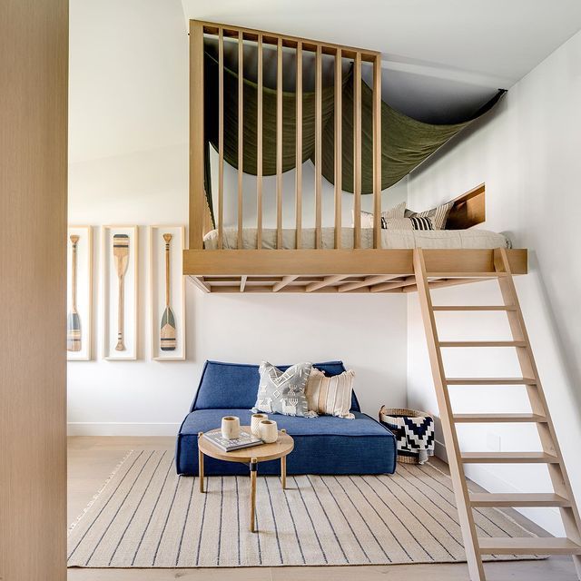 a living room with a blue couch under a loft bed next to a wooden staircase