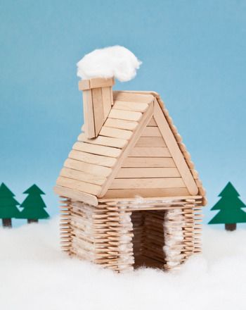 a small house made out of wooden sticks and snow on the roof, with trees in the background