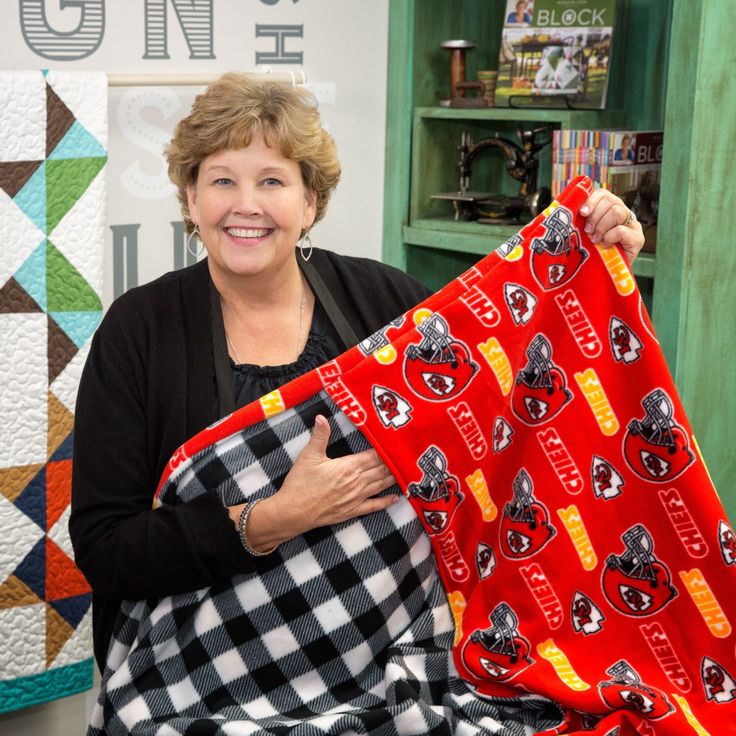 a woman is holding up a red and black blanket in front of some quilts