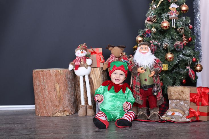 there is a small child sitting in front of the christmas tree and other decorations on the floor