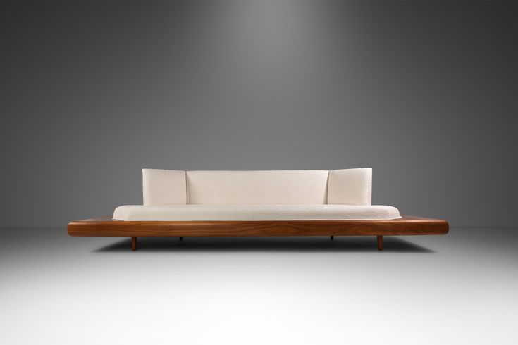 a white couch sitting on top of a wooden frame in front of a gray wall