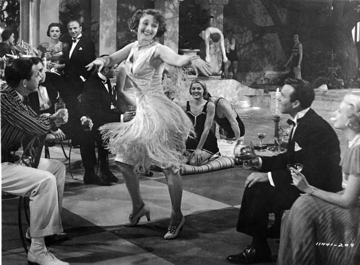 an old photo of some people dancing in the middle of a dance floor with other people sitting around