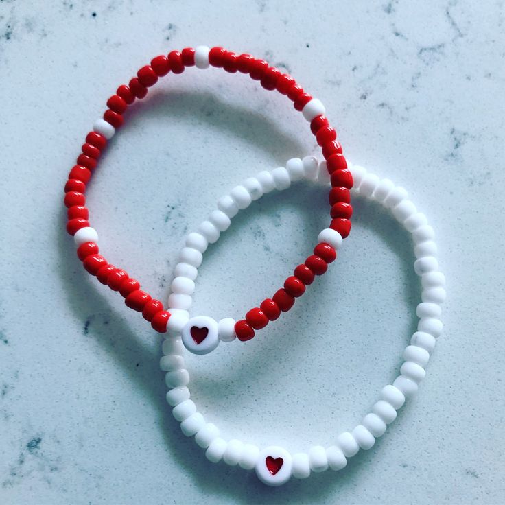 two red and white beaded bracelets with hearts on them sitting on a table