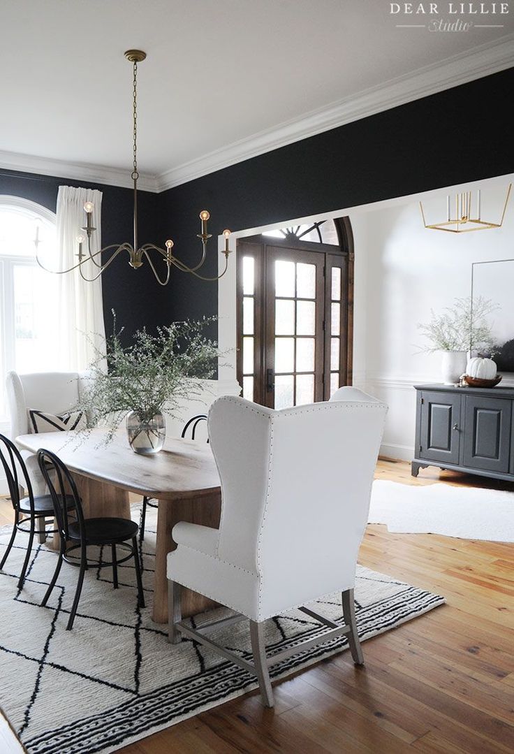 an elegant dining room with black walls and white chairs, wood flooring, and chandelier