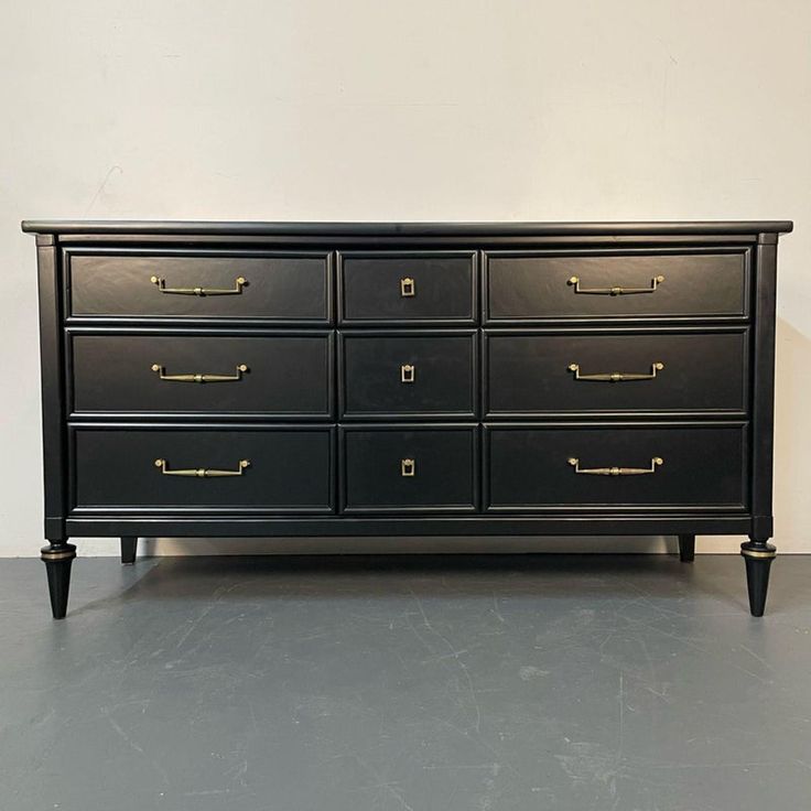 a large black dresser with gold handles on it's legs and drawers, against a white wall