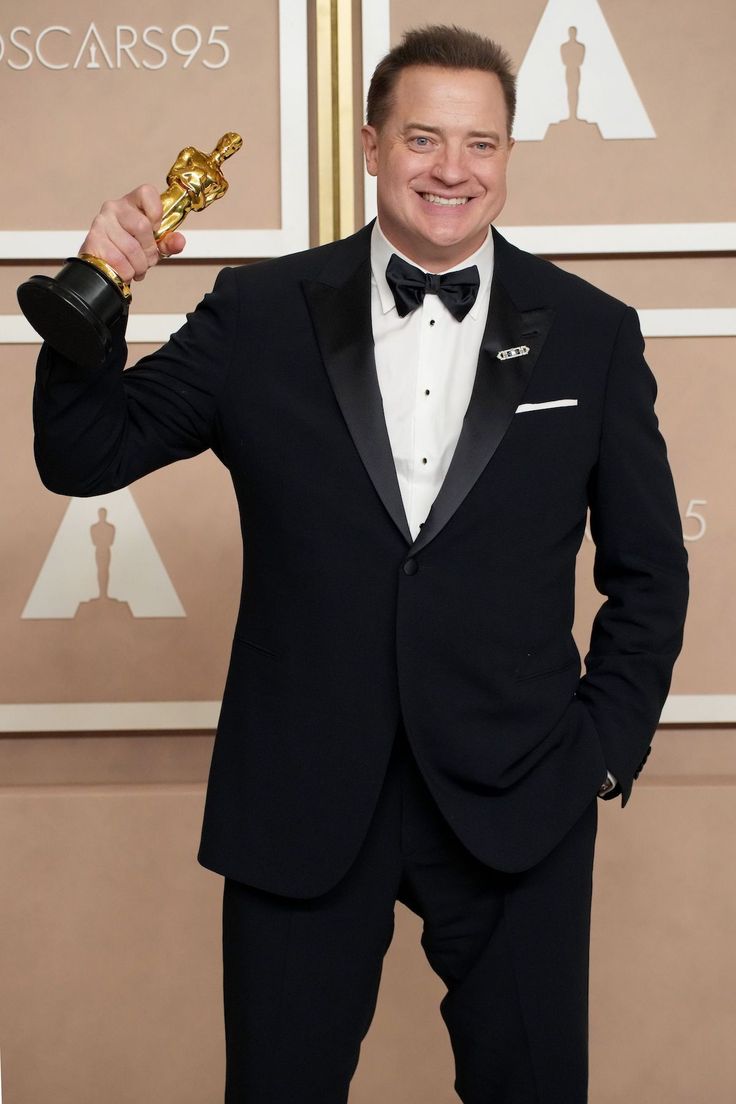 a man in a tuxedo holding an award for best performance by an actor