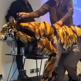 two men standing next to each other in front of a large stuffed tiger on a stage