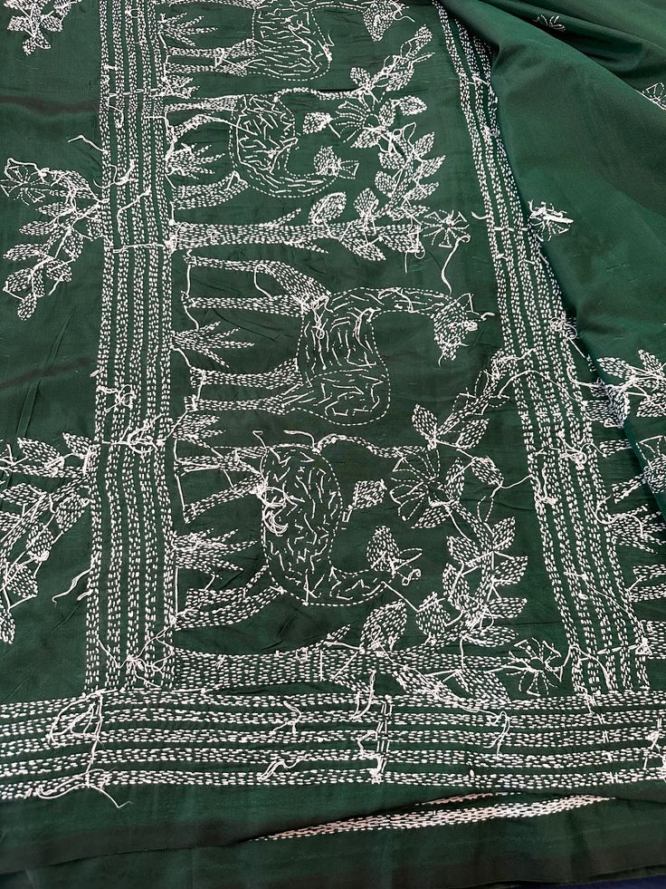 a green table cloth with white embroidered designs on it, sitting on a blue surface