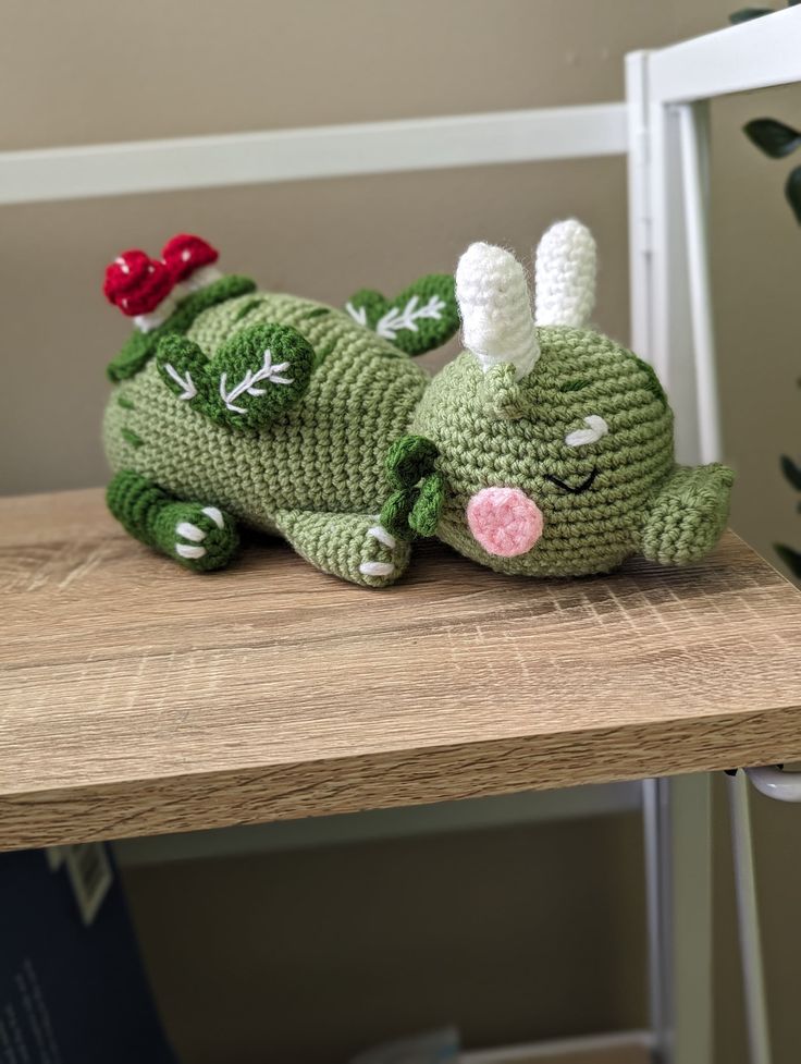 a crocheted green dragon laying on top of a wooden table