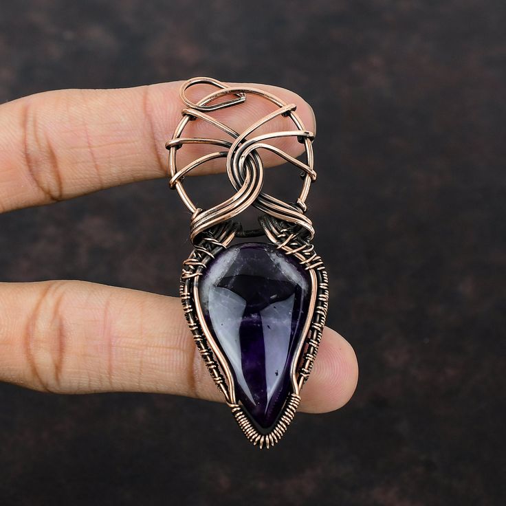 Note : Due to the natural formation of this gemstone. Slight variation in design and color are to be expected. Chevron Amethyst Pendant Copper Wire Wrapped Pendant Elegant Pendant Gemstone Pendant Wire Wrap Jewelry Gift For Her Handmade Copper Jewelry Handmade Copper Pendant SKU : VFWP-720 Gemstone : Chevron Amethyst Stone Shape : Pear    Metal Purity : Copper Pendant Length : 80 MM   Pendant Width : 30 MM Chevron Amethyst combines the metaphysical powers between Quartz and the stress-relieving properties of Amethyst, lessening ones resistance on your path to self-discovery. This stone is often said to be stronger and more powerful, especially with higher chakras, focusing often on the third eye and crown chakras. Teardrop Amethyst Jewelry With Natural Stones, Artisan Purple Gemstone Jewelry, Purple Amethyst Amulet Jewelry, Artisan Purple Amethyst Jewelry, Unique Amethyst Gemstone Bead Jewelry, Teardrop Amethyst Bead Jewelry, Teardrop Amethyst Gemstone Beads Jewelry, Amethyst Gemstones For Jewelry Making In Teardrop Shape, Amethyst Round Pendant Jewelry With Natural Stones