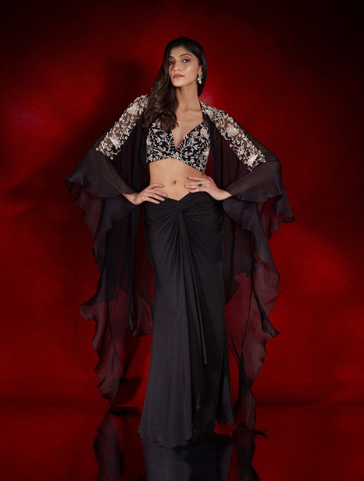 Black satin georgette draped skirt paired with champagne & silver floral embellished bralette & a flowy georgette and organza cape with hand-embellished sheer shoulder panels.From Shloka Khialani's Winter Sun collection.DELIVERY TIMEPlease allow 6-8 weeks for your outfit to arrive.FABRIC DETAILSGeorgette, Satin Geotgette, NetProfessional cleaning only. Festive Party Wear Sets With Draped Sleeves, Glamorous Floor-length Georgette Sets, Party Wear Sets With Draped Sleeves For Reception, Glamorous Sets With Sheer Dupatta In Georgette, Evening Cape Sets Made Of Georgette, Evening Party Wear Sets With Cape Sleeves, Party Wear Sets With Cape Sleeves For Evening, Evening Sets With Cape Sleeves For Party Wear, Festive Evening Set With Cape Sleeves