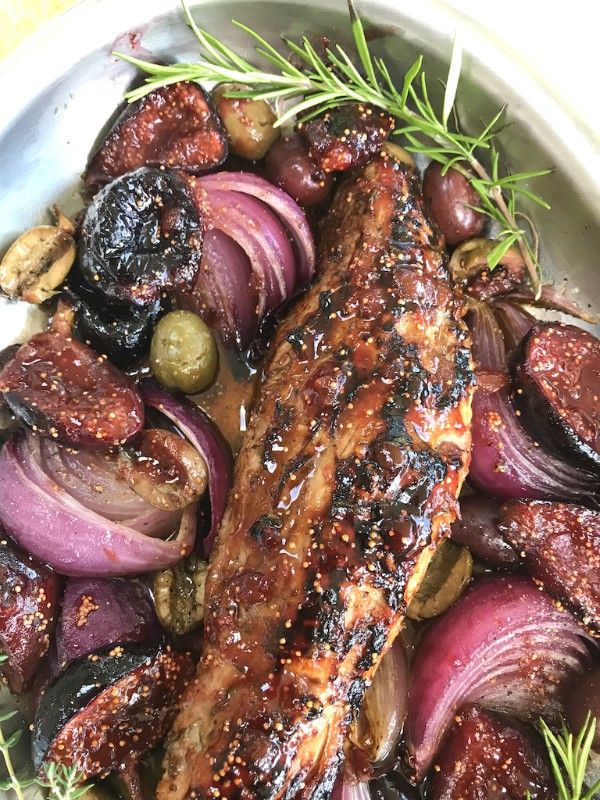 a plate with meat, onions and olives on it next to some rosemary sprigs