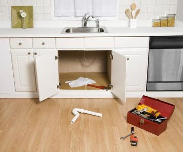 an open cabinet in the middle of a kitchen with tools on the floor next to it