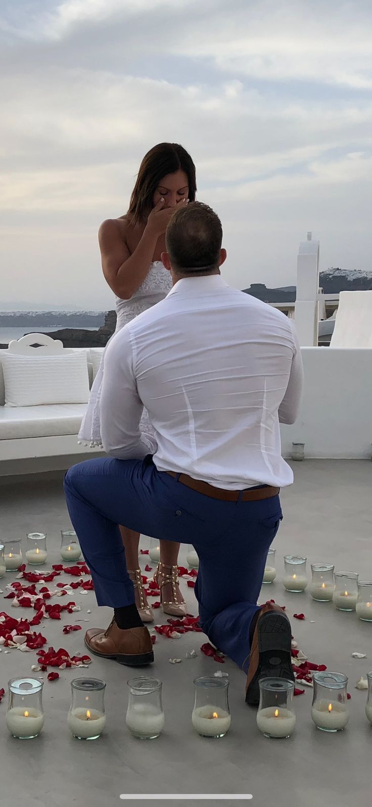 a man kneeling down next to a woman on top of a roof covered in candles