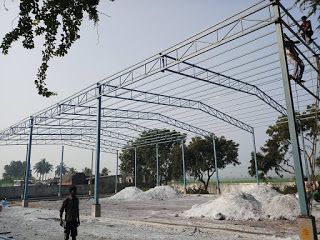 a man walking down a dirt road under a metal structure