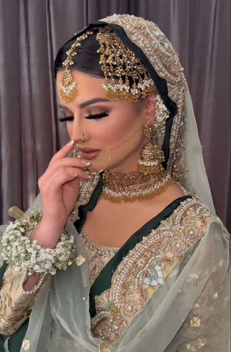 a woman in a bridal gown with jewelry on her head and hands to her face