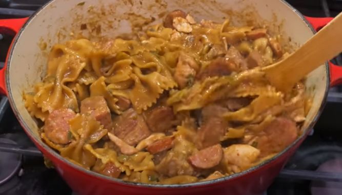 a red pot filled with pasta and meat on top of an open flamed stove