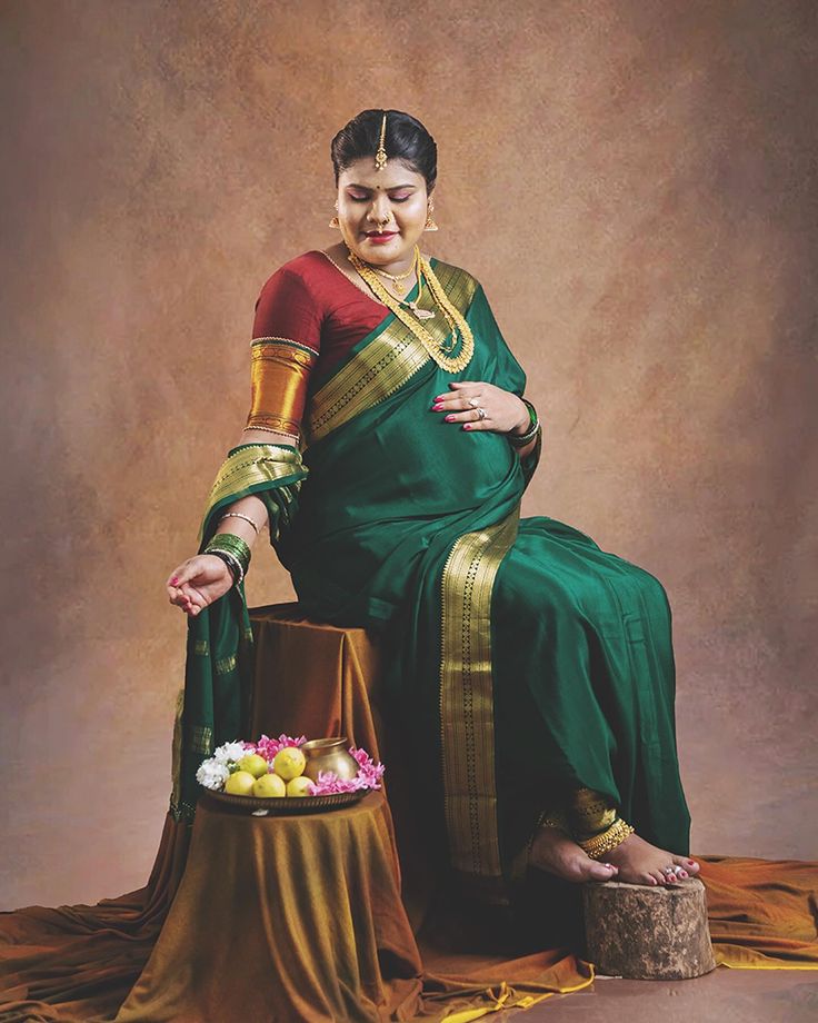 a woman in a green and gold sari sitting next to a basket of fruit