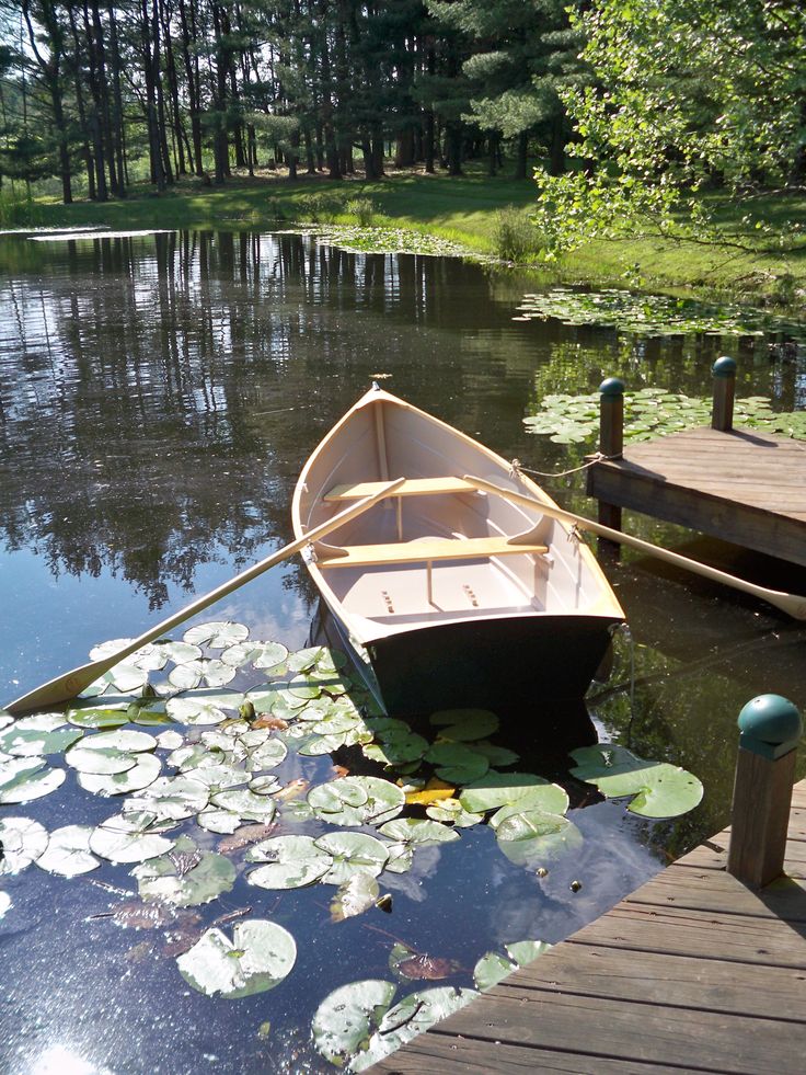 a small boat floating on top of a lake next to a wooden dock with lily pads