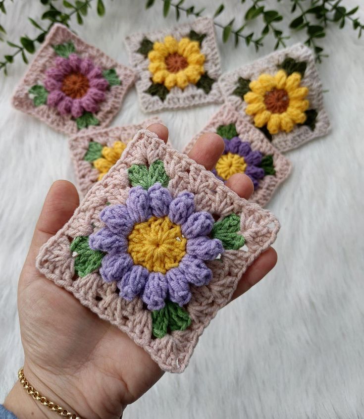 a hand holding four crocheted coasters with flowers on them