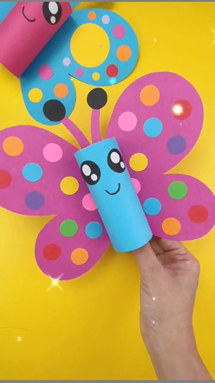 a hand holding a paper butterfly on top of a yellow surface with polka dot dots