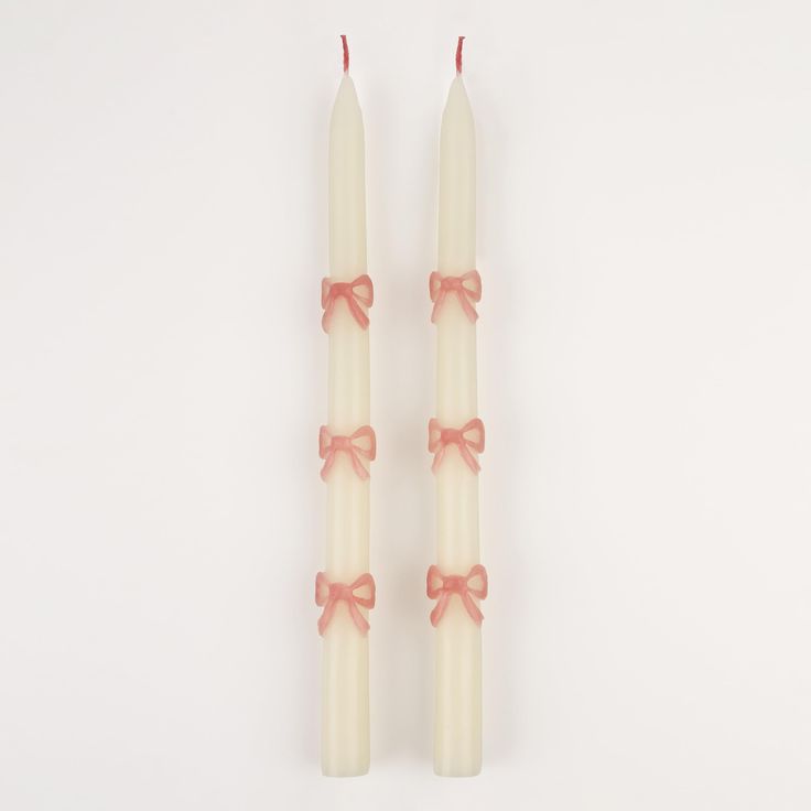 two white candles with pink bows on them