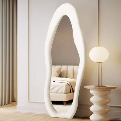 a large white mirror sitting on top of a wooden floor next to a table and lamp