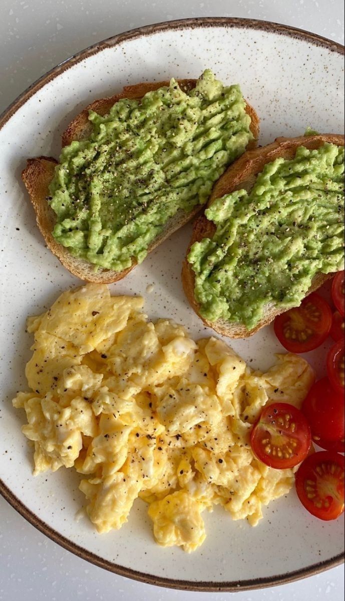 two pieces of toast with avocado and tomatoes on it sitting on a plate