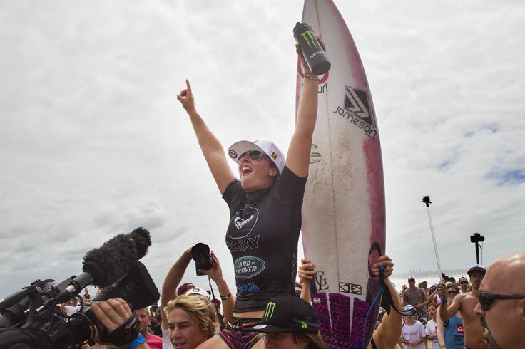 a woman is holding up her surfboard in the air while others are taking pictures