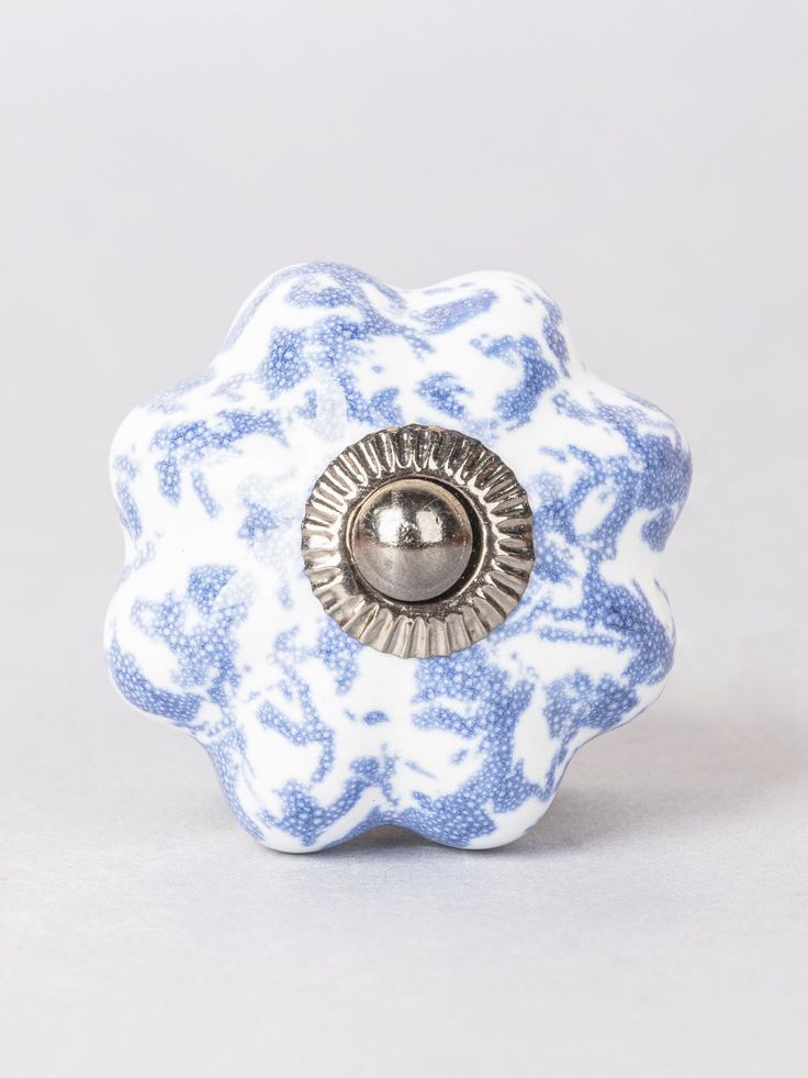 a blue and white flower shaped object with a metal button in the center on a gray background