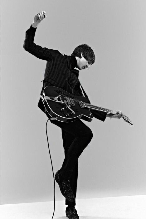 a man holding a guitar while standing on top of a white floor next to a microphone