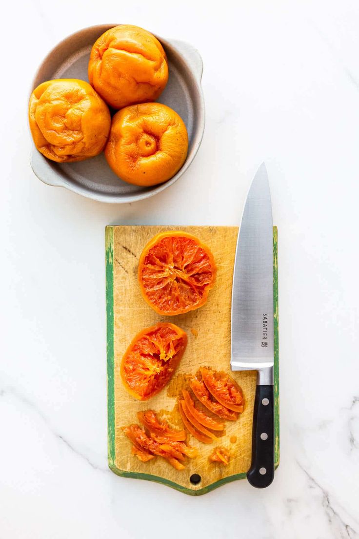 tomatoes on a cutting board next to a knife and bowl with peeled tomatoes in it