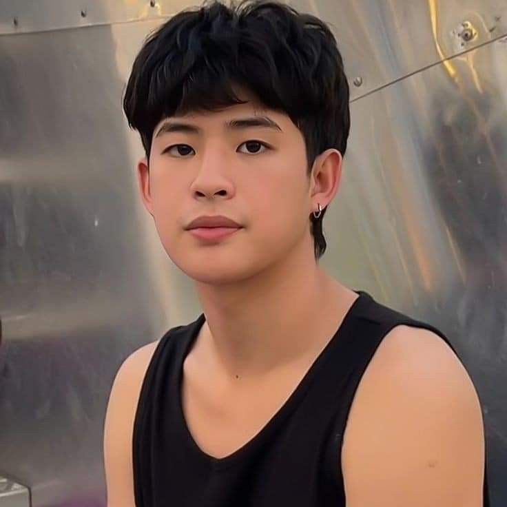 a young man standing in front of a metal structure wearing a black tank top and looking at the camera