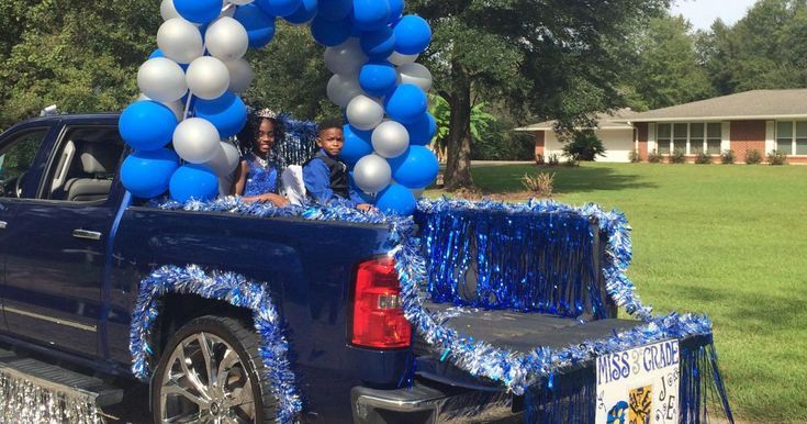 two people sitting in the back of a truck decorated with blue and silver balloons,