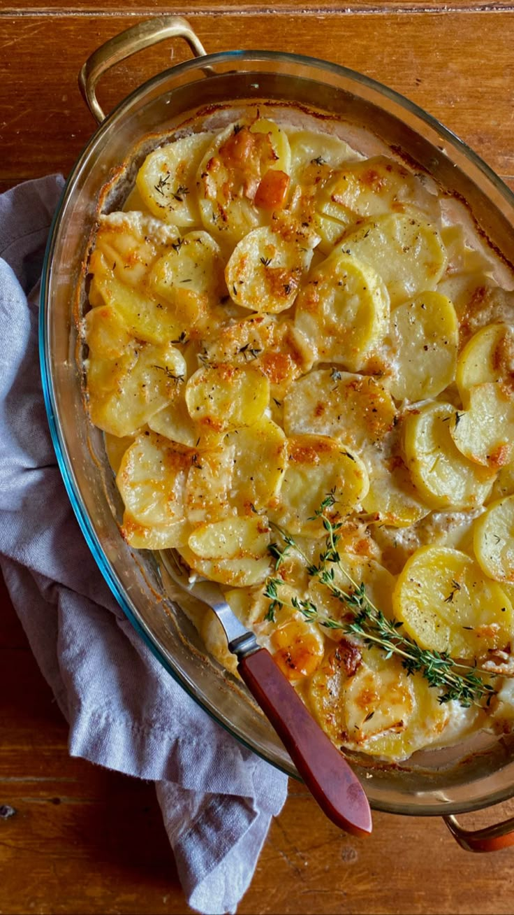 a casserole dish with potatoes and herbs in it on a wooden table next to a napkin