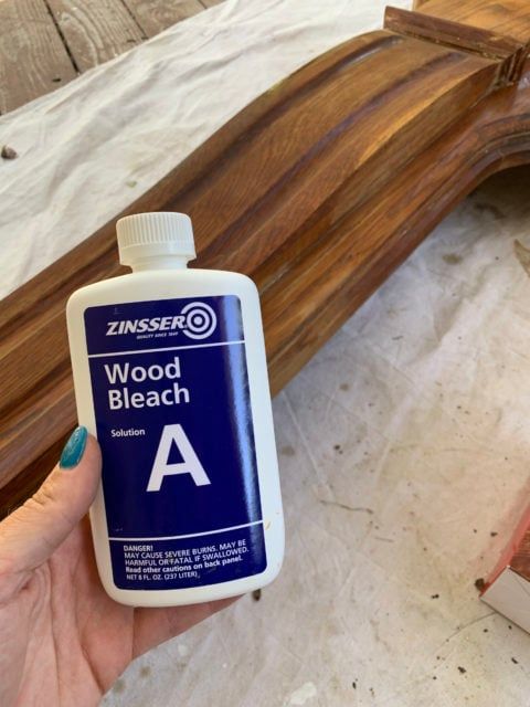 a hand holding a bottle of wood bleach next to a piece of wood