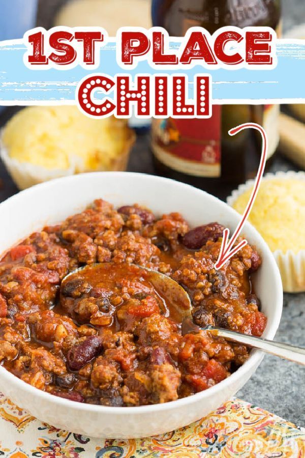 a white bowl filled with chili and topped with a spoon next to muffins