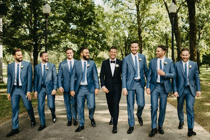 a group of men standing next to each other wearing blue suits and bow ties in front of trees