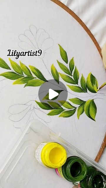 an embroidery project with green leaves on it and yellow paint in the middle next to some scissors