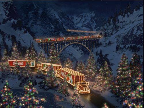 a train traveling through a snow covered forest next to a christmas tree filled mountain range