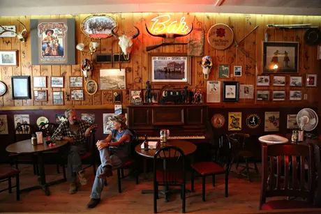 two men sitting at tables in a restaurant with many pictures on the wall behind them